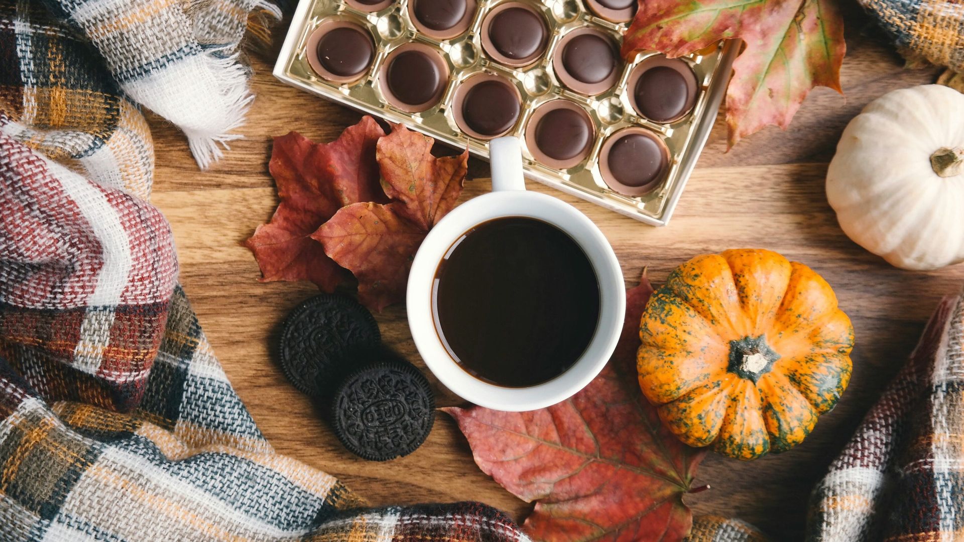 Tasse de café, chocolats, biscuits, citrouilles et feuilles d’automne sur une table avec un plaid — ambiance cosy de lecture